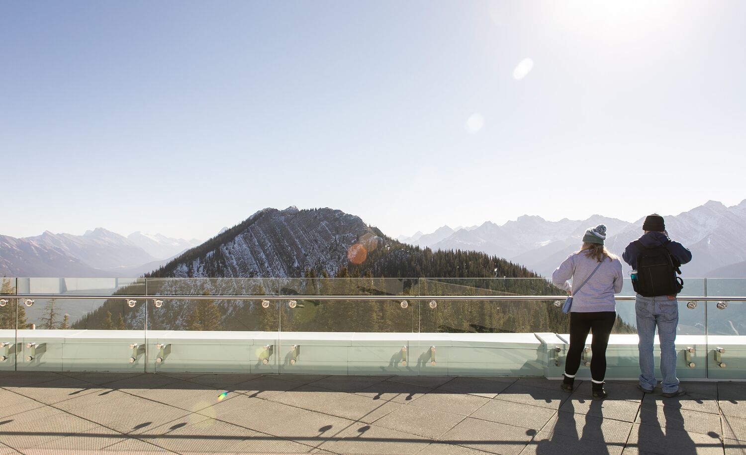 Two people look over the edge at the Banff Gondola with a mountain in the background.